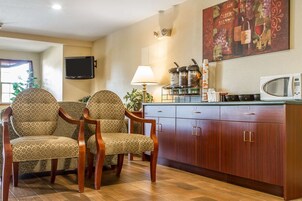 A dining area with two patterned chairs, a wooden cabinet, a microwave, and a wall-mounted TV.