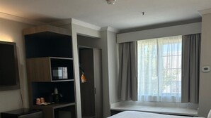 Ein Hotelzimmer mit zwei Betten, einem Schreibtisch, einer Minibar und einem Fenster mit Vorhängen.