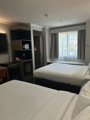 Habitación de hotel con dos camas, un escritorio, un minibar y un ventanal con cortinas.