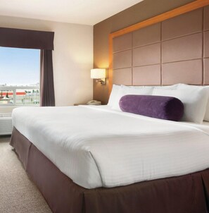 A hotel room with a large bed, a nightstand with a lamp, a window with curtains, and a view of the outside.