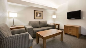 A hotel room with a sofa, two armchairs, a wooden coffee table, a TV, and a small cabinet. - Days Inn Calgary Airport (Calgary)