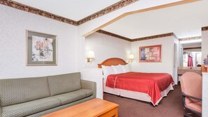 Una habitación de hotel con una cama, un sofá, una mesita y dos lámparas adosadas a la pared.