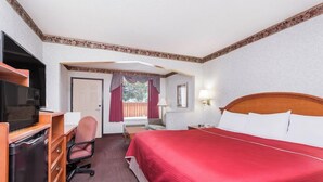 Una habitación de hotel con cama, escritorio, silla, televisor y ventana con cortinas.