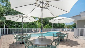 An outdoor patio with a pool, surrounded by a white fence, featuring green chairs and large umbrellas. - Sleep Inn & Suites Panama City Beach East (Panama City Beach)