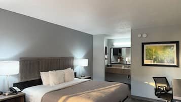 A hotel room with a bed, bedside lamps, a desk with a chair, a mirror, and a painting on the wall.