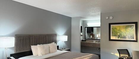 Quarto de hotel com cama, abajures, escrivaninha com cadeira, espelho e um quadro na parede.