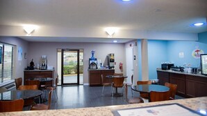 Un comedor de hotel con mesas, sillas, una máquina de café y un televisor.