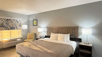 A hotel room with a bed, two bedside tables, a chair, a wall-mounted heater, and a decorative wall panel.