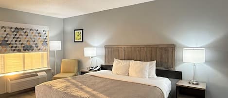 A hotel room with a bed, two bedside tables, a chair, a wall-mounted heater, and a decorative wall panel.