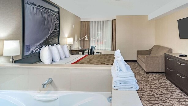 Una habitación de hotel con una cama grande, un sofá, un escritorio, un televisor y un baño con bañera y lavabo.