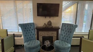 Una habitación con dos sillones azules, chimenea, televisor de pantalla plana y un ventanal con persianas.