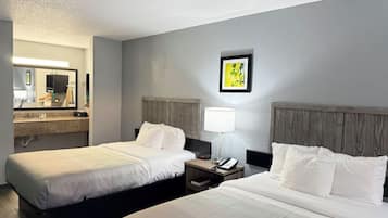 A hotel room with two beds, a nightstand with a lamp, a mirror, and a painting on the wall.