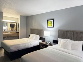 A hotel room with two beds, a nightstand with a lamp, a mirror, and a painting on the wall.