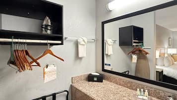 A hotel bathroom with a granite countertop, a sink, a mirror, a towel rack, and a clothing rack with a 'Choice Privilege' sign.