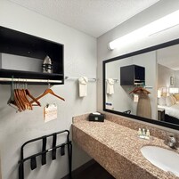 A hotel bathroom with a granite countertop, a sink, a mirror, a towel rack, and a clothing rack with a 'Choice Privilege' sign.
