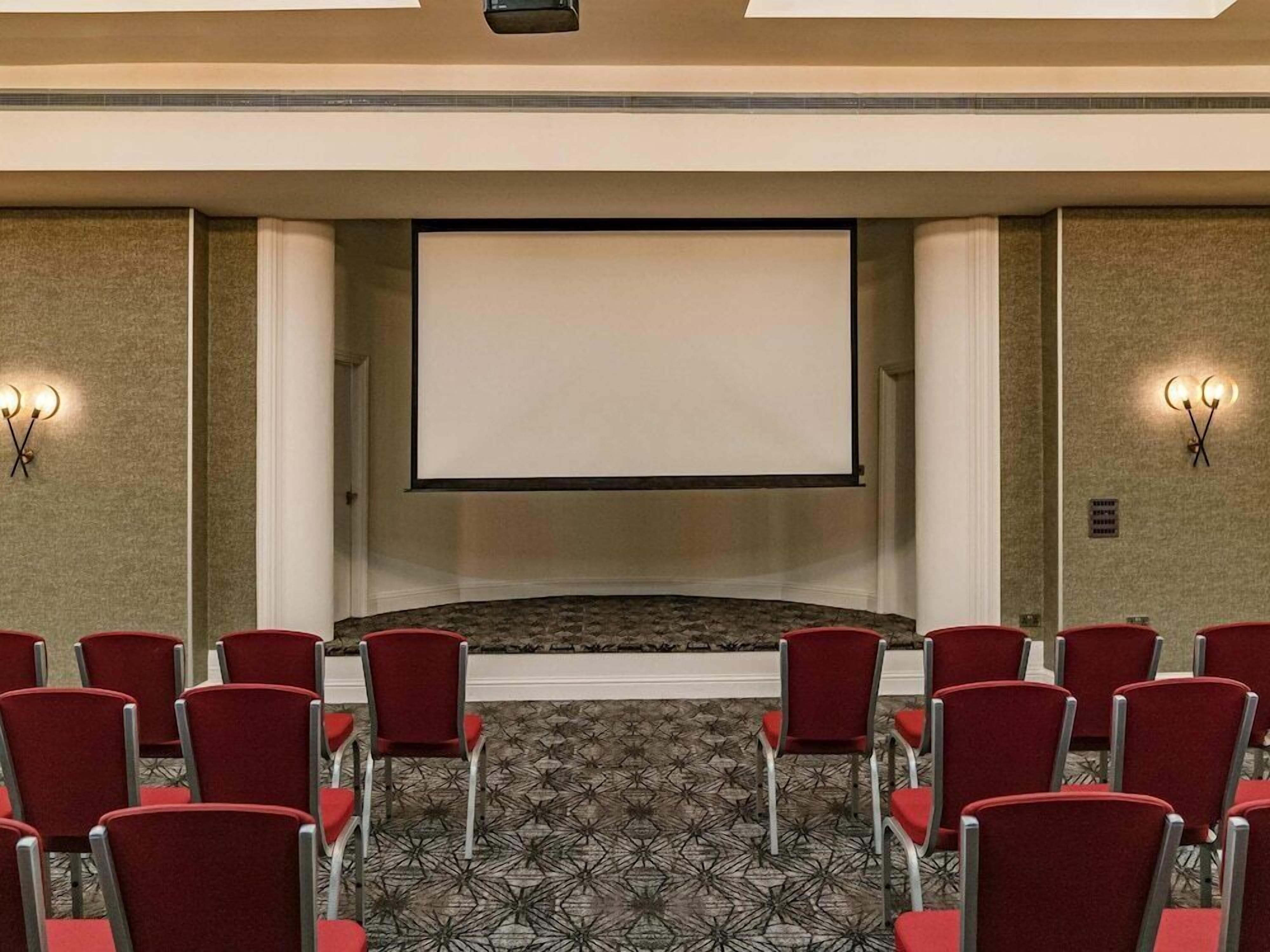 A conference room with a large screen, red chairs, and patterned carpet.