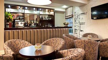 A bar area with a mirrored wall, patterned seating, and a television mounted on the wall.