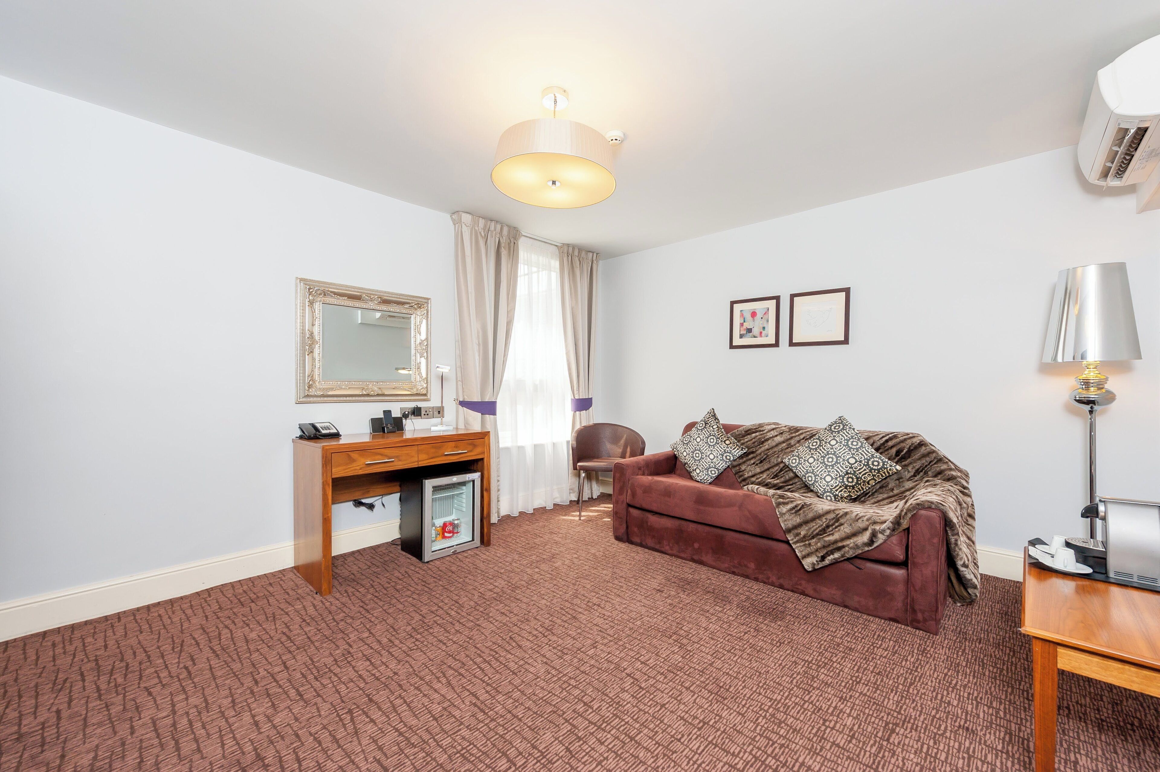 A room with a brown sofa, a desk with a telephone, a mirror, and a lamp.