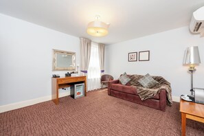 Ein Zimmer mit einem braunen Sofa, einem Schreibtisch mit Telefon, einem Spiegel und einer Lampe.