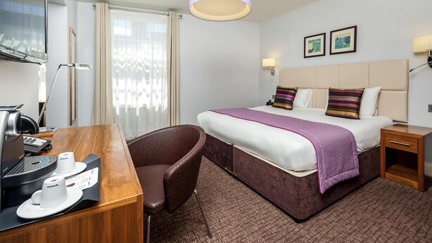 A hotel room with a bed, a desk with a coffee machine, a chair, a TV, and a window with curtains. - Nottingham City Centre Hotel by Sunday (Nottingham)