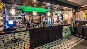Una zona de bar con mostrador, estantes llenos de botellas, luces colgantes y un suelo estampado.