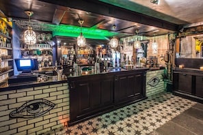 A bar area with a counter, shelves with bottles, hanging lights, and a patterned floor.