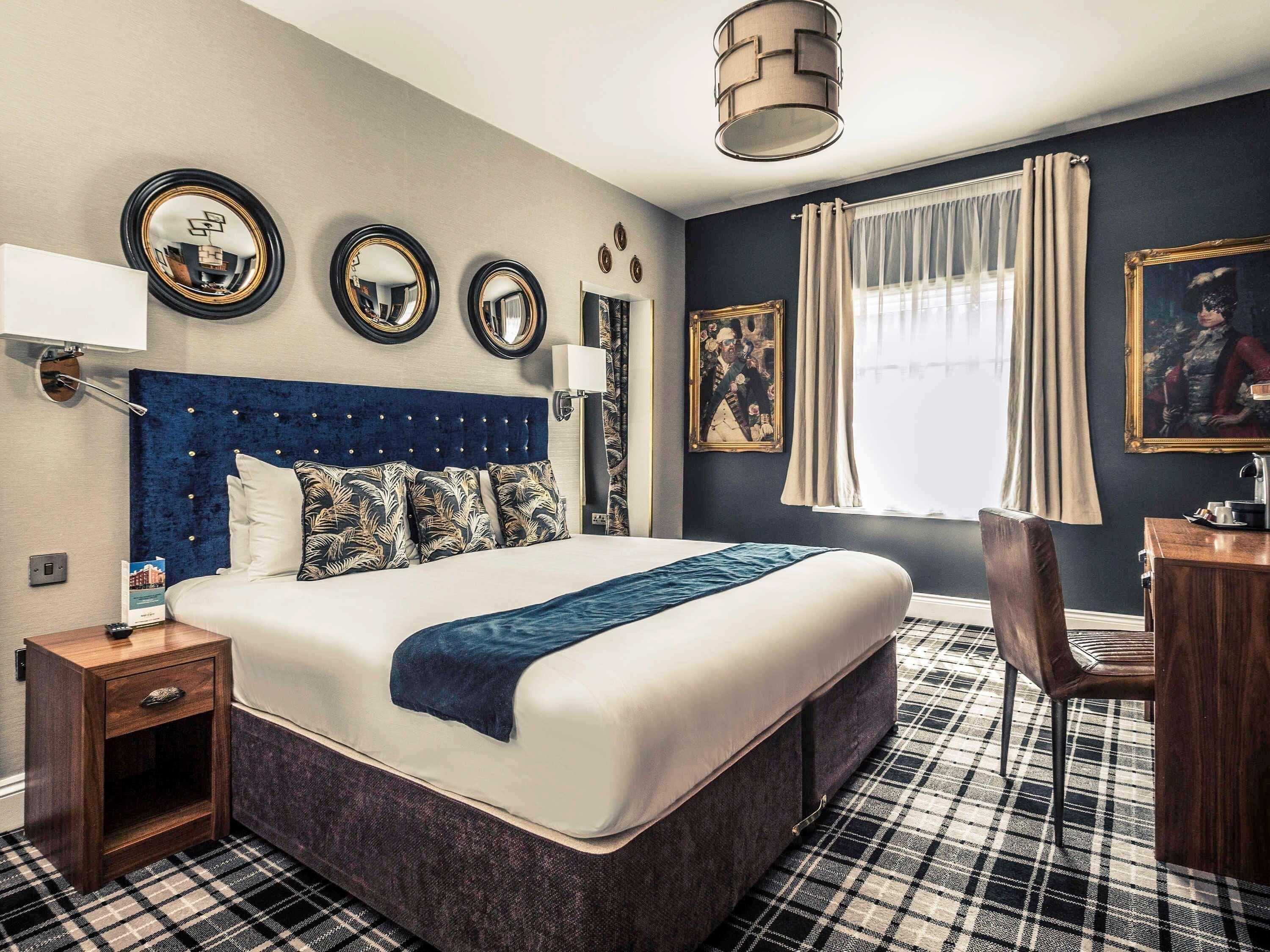 A hotel room with a large bed, a desk, a chair, and a window with curtains.