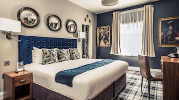 A hotel room with a large bed, a desk, a chair, and a window with curtains.