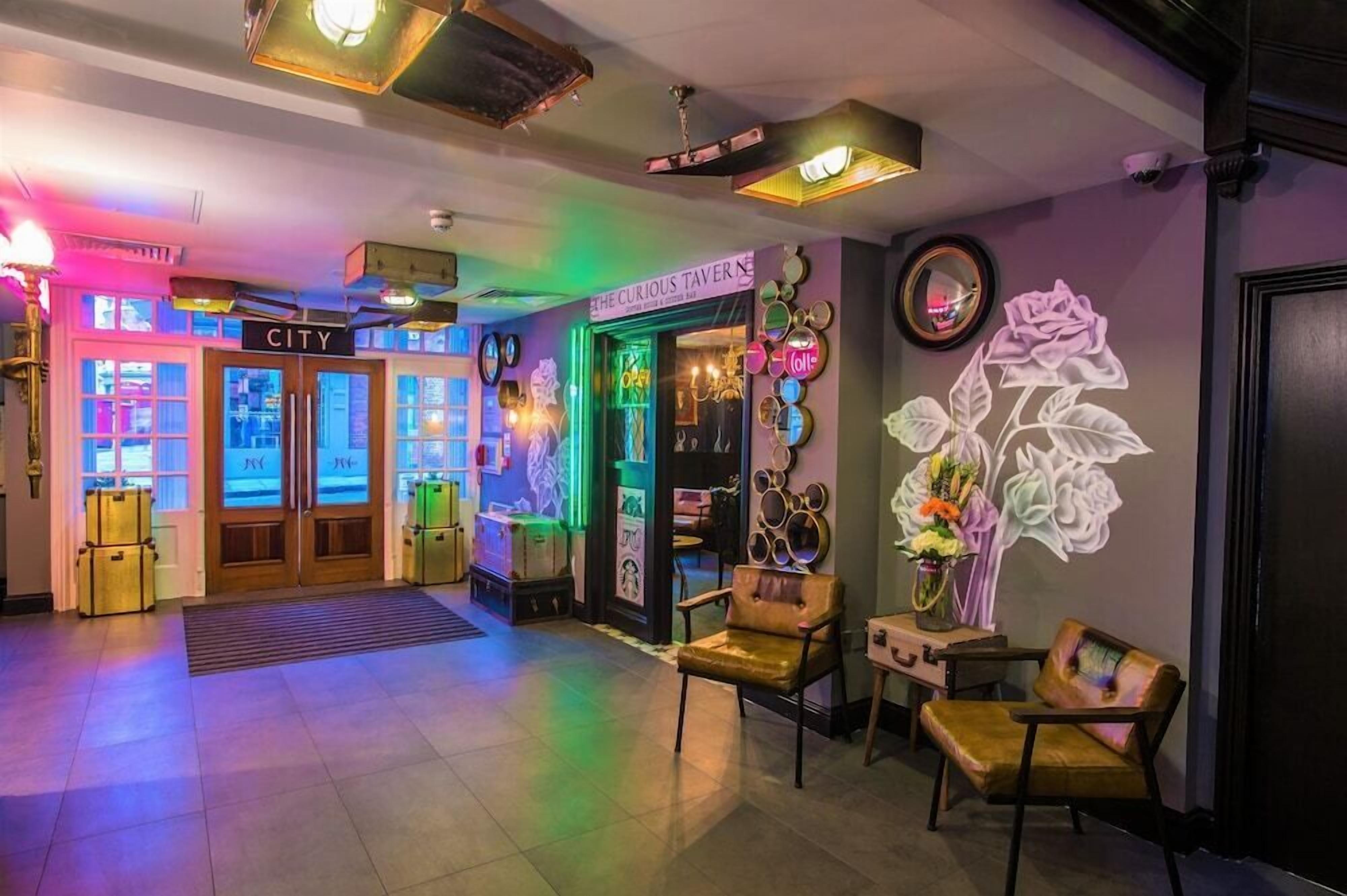 A hotel lobby with a neon sign for 'The Curious Tavern,' a reception desk, and a wall with a large floral mural.