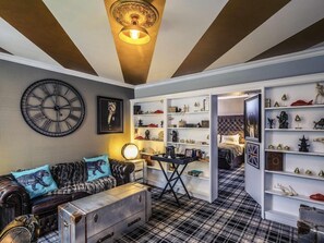 Een kamer met een grote wandklok, een bank met gestreepte kussens, een koffer en een plank met diverse spullen.