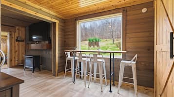 Een houten hut interieur met een bar, een televisie en een groot raam dat uitkijkt op een tuin.