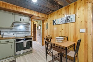 A kitchen with wooden walls, a stainless steel oven, and a table with chairs.