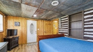 Een blokhutkamer met een bed, een televisie en een raam in de deur.