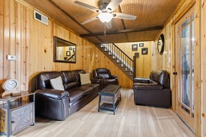 A wooden interior with a ceiling fan, leather sofas, a staircase, and a large mirror.