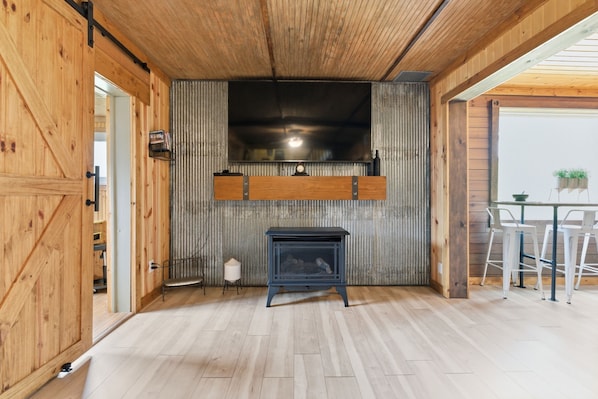 Ein rustikales Interieur mit Holzbalkendecke, integriertem Fernseher, Kamin und Essbereich mit Stühlen.