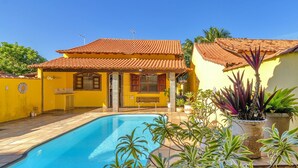 Una casa con piscina, techo de tejas y plantas en macetas.