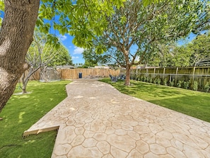 A stone pathway leading to a backyard with a wooden fence, a tree, and a clear sky. - Spacious 4-bedroom home in peaceful Miami Springs - Sleeps 14 (Miami Springs)