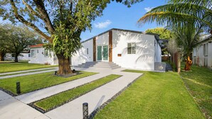 Ein modernes, zweistöckiges Haus mit weißer Fassade, einem Eingangsbereich mit Treppe und einem gepflegten Rasen.