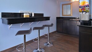 A modern kitchen with a black countertop, three bar stools, a juice dispenser, and a mirror on the wall. - Emerald Inn on Sunset (Los Angeles)