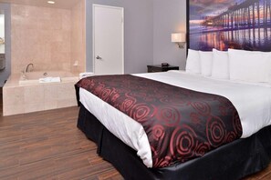 A hotel room with a large bed, a bathtub, and a wall-mounted lamp. - Emerald Inn on Sunset (Los Angeles)