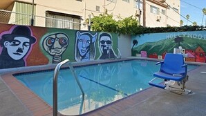 A swimming pool with a mural on the wall, a blue lounge chair, and a 'Hollywood' sign in the background. - Emerald Inn on Sunset (Los Angeles)