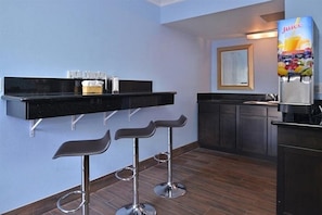 A modern kitchen with a black countertop, three bar stools, a juice dispenser, and a framed picture on the wall. - Emerald Inn on Sunset (Los Angeles)