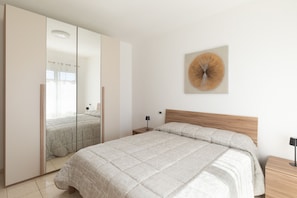Ein Schlafzimmer mit Bett, Nachttisch, Lampe, Spiegel und einem Wandbild.
