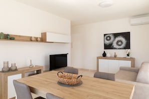 Ein modernes Wohnzimmer mit einem Holzesstisch, grauen Sofas, einem Flachbildfernseher und einem an der Wand befestigten Kunstwerk.