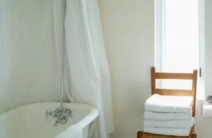 Ein Badezimmer mit Dusche, Waschbecken, einem Stuhl und Handtüchern sowie einem Fenster.
