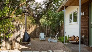 Un espacio al aire libre techado con una parrilla, dos sillas y una pila de leña.