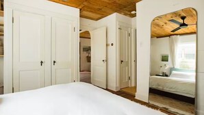 Un dormitorio con una cama grande, paredes blancas, vigas de madera en el techo y un ventilador de techo.
