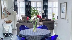 Ett modernt vardagsrum med ett runt bord, blå stolar, en soffa och en matplats.