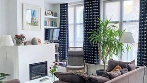 Ett vardagsrum med en soffa, fåtölj, soffbord, bokhylla och en stor växt.