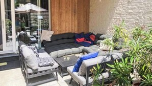 En modern utomhusplats med sittmöbler, bestående av en soffa, stolar och ett bord, omgiven av växter och en stenmur.
